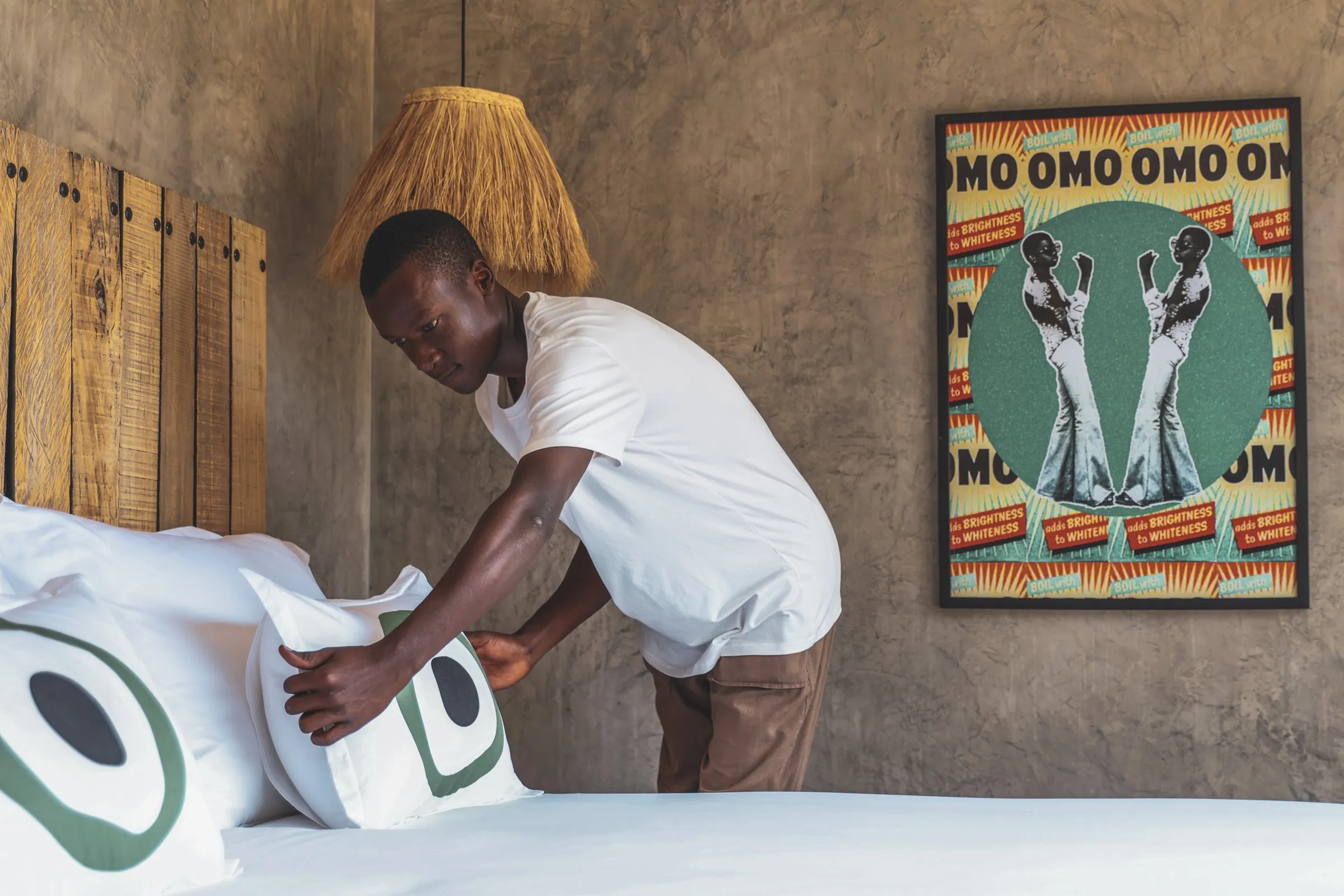 Housekeeping making a bed in a cabin, Omo Omo artwork on the wall