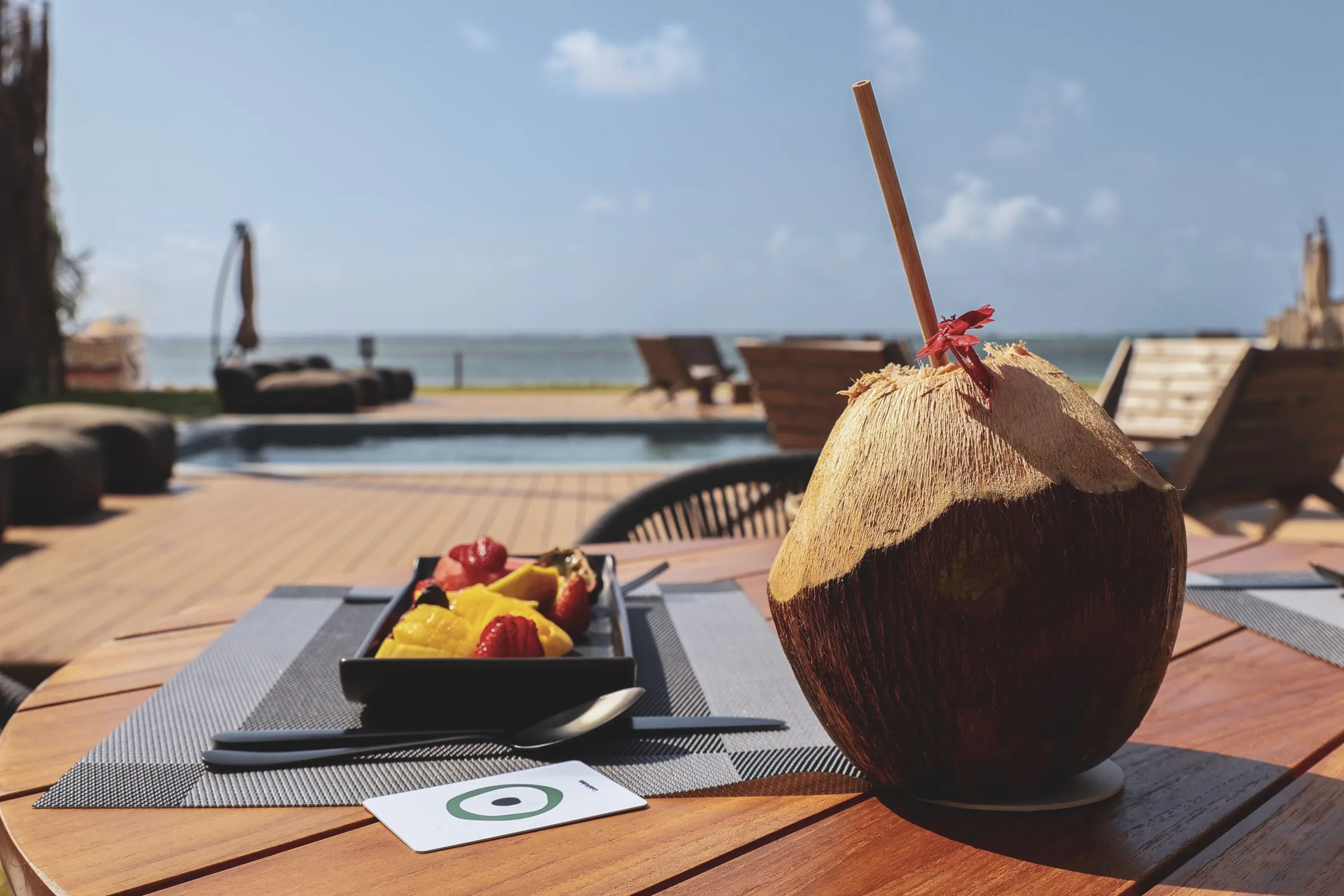 A coconut on the table, the pool and sea beyond